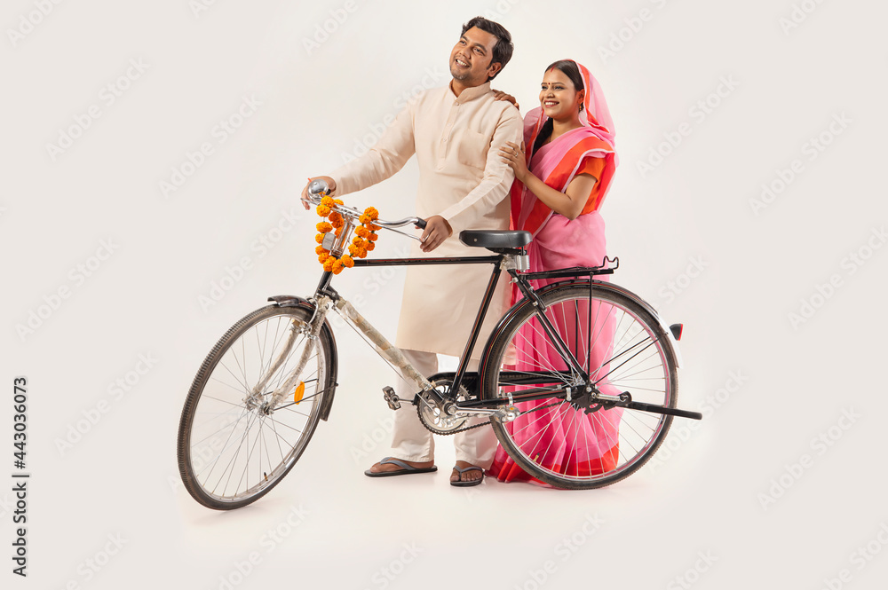 A RURAL COUPLE LOOKING AWAY WHILE STANDING WITH NEW BICYCLE
