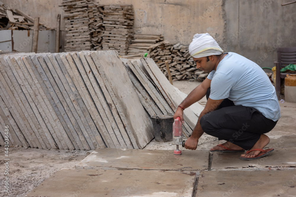 A LABOURER WORKING ON TILE WITH ELECTRIC EQUIPMENT A LABOURER WORKING ON TILE WITH ELECTRIC EQUIPMENT