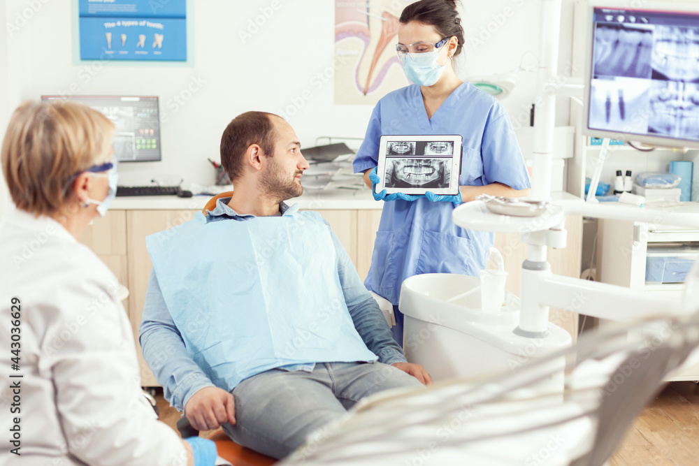 Obraz premium Medical nurse showing on tablet teeth x-ray showing it with patient. Dentist senior doctor and nurse working together in modern stomatological clinic, explaining treatment to man patient