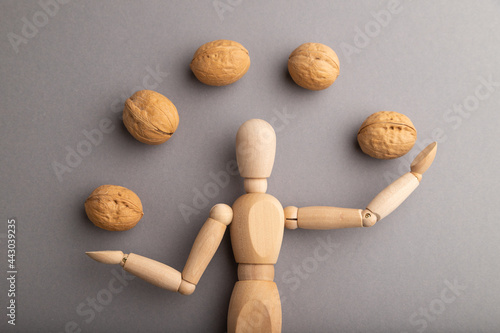 Wooden mannequin juggling walnuts on gray pastel background. close up.