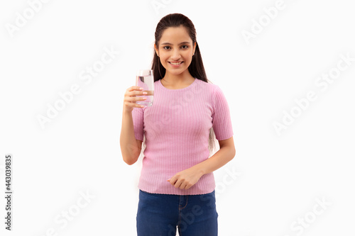 PORTRAIT OF A TEENAGE GIRL STANDING WITH A GLASS OF WATER IN HAND