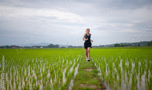 Young sporty girl running on a rural road at sunset in summer field. 