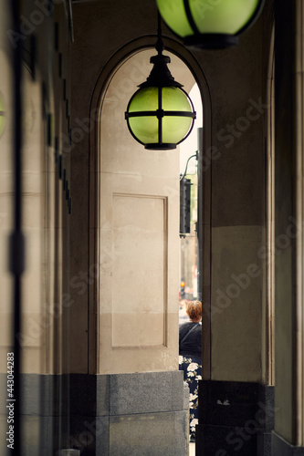 Looking down covered passageway next to contemporary luxury arcade building showing vertical lines, partial view of one person and ornate light