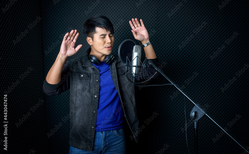 Φωτογραφία Young asian man dance, swaying, and lifting his arms rhythmically while singing in front of black soundproofing wall