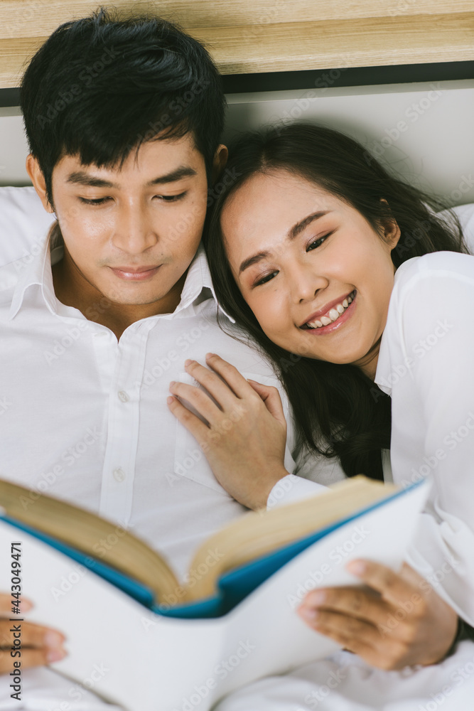 Young happy attractive Asian couple lying together in bed reading book. Concept for love and happy relationship Young happy attractive Asian couple lying together in bed reading book. Concept for love and happy relationship