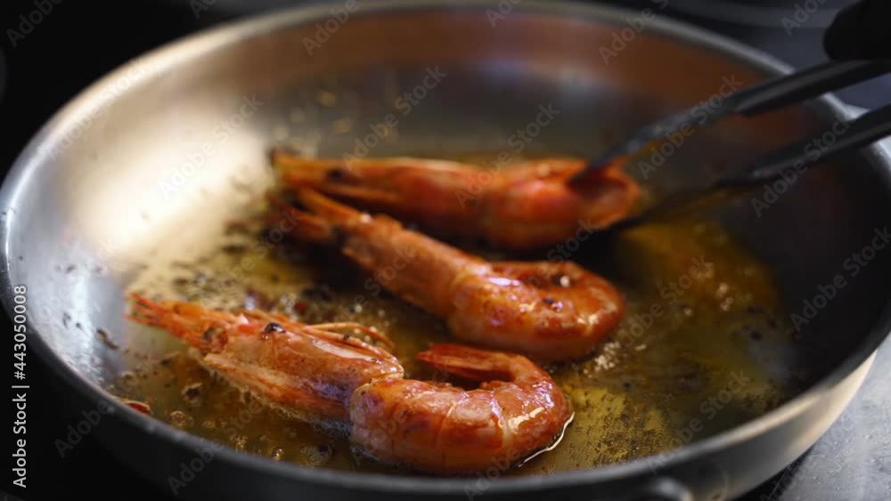 Cook turns shrimps with forceps on a grill. Closeup of king prawns frying in a pan. Chef frying royal shrimps on a hot pan. Macro sea food preparation. Cook turns shrimps with forceps on a grill. Closeup of king prawns frying in a pan. Chef frying royal shrimps on a hot pan. Macro sea food preparation.