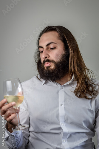 portrait of a young middle eastern businessman with beard and long hair holding a glass of fresh white wine and looking at its color 