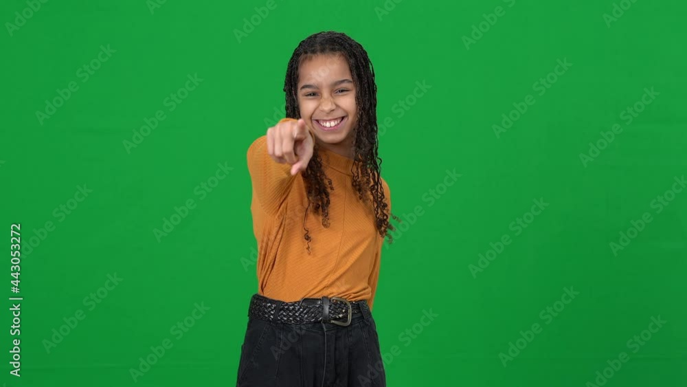 Laughing African American teen girl grimacing gesturing on green screen mocking. Portrait of adolescent bully sneering on chromakey background pointing at camera. Adolescence concept Laughing African American teen girl grimacing gesturing on green screen mocking. Portrait of adolescent bully sneering on chromakey background pointing at camera. Adolescence concept