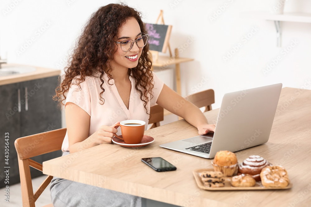Beautiful young woman with cup of coffee using laptop in kitchen Beautiful young woman with cup of coffee using laptop in kitchen