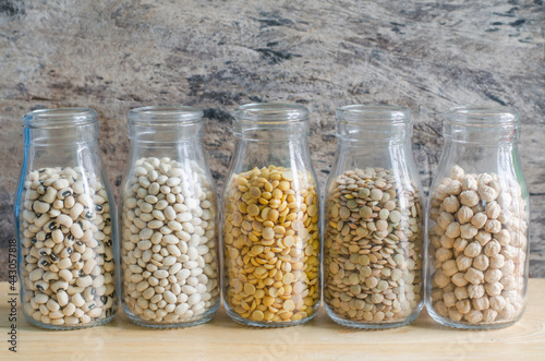 Five kinds of dry organic cereal and grain seed in glass bottle on white background, consisted of blackeye pea, white and mung bean, lentils and chick pea on wooden background, ready for cooking