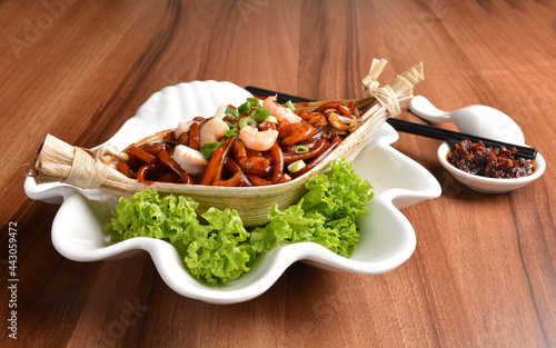 stir fried hokkien dark soy sauce udon noodle with seafood and meat in leaf on wood table asian halal menu photo