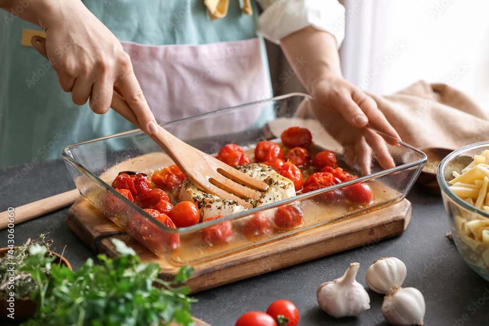 Woman preparing tomatoes and feta cheese in kitchen