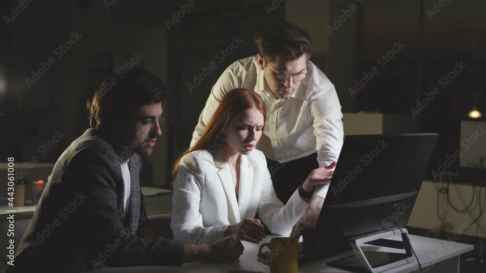 A hardworking woman works late at the office with colleagues. Office employees solve work tasks in the night office A hardworking woman works late at the office with colleagues. Office employees solve work tasks in the night office