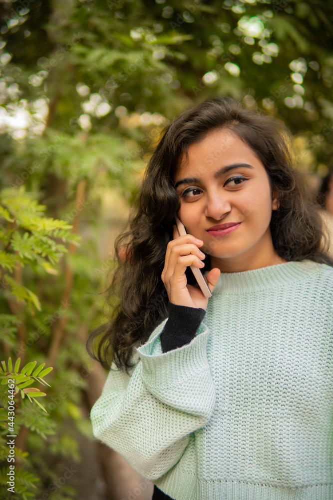 Outdoor image of an Asian, Indian beautiful happy young woman talking on smartphone in park and enjoying the fresh air at day time. Outdoor image of an Asian, Indian beautiful happy young woman talking on smartphone in park and enjoying the fresh air at day time.