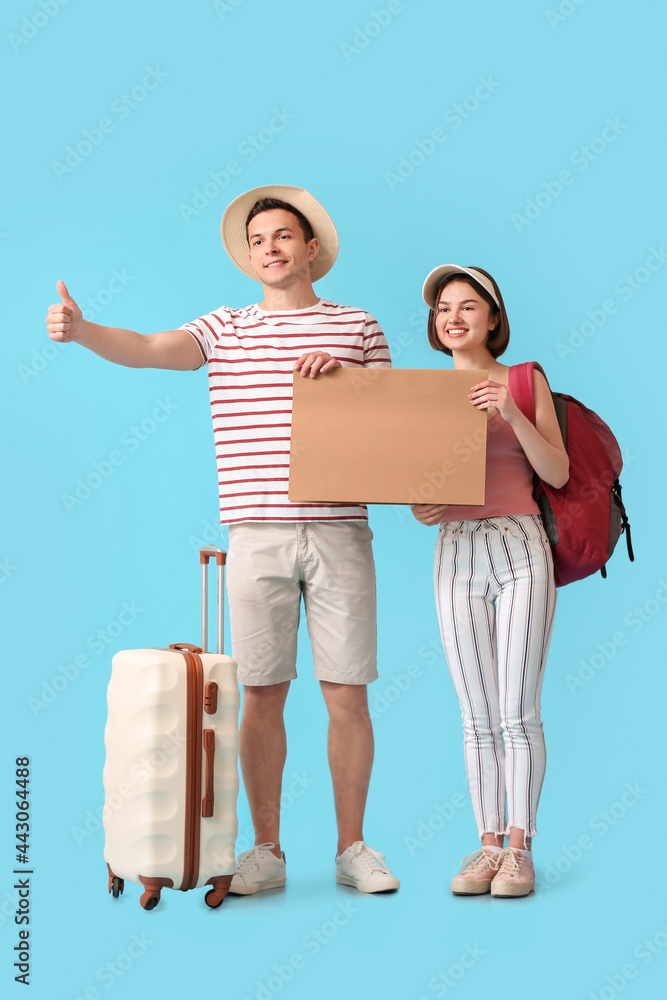 Young couple with cardboard hitchhiking on color background