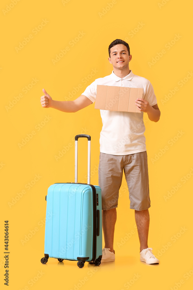 Young man with cardboard and suitcase hitchhiking on color background Young man with cardboard and suitcase hitchhiking on color background