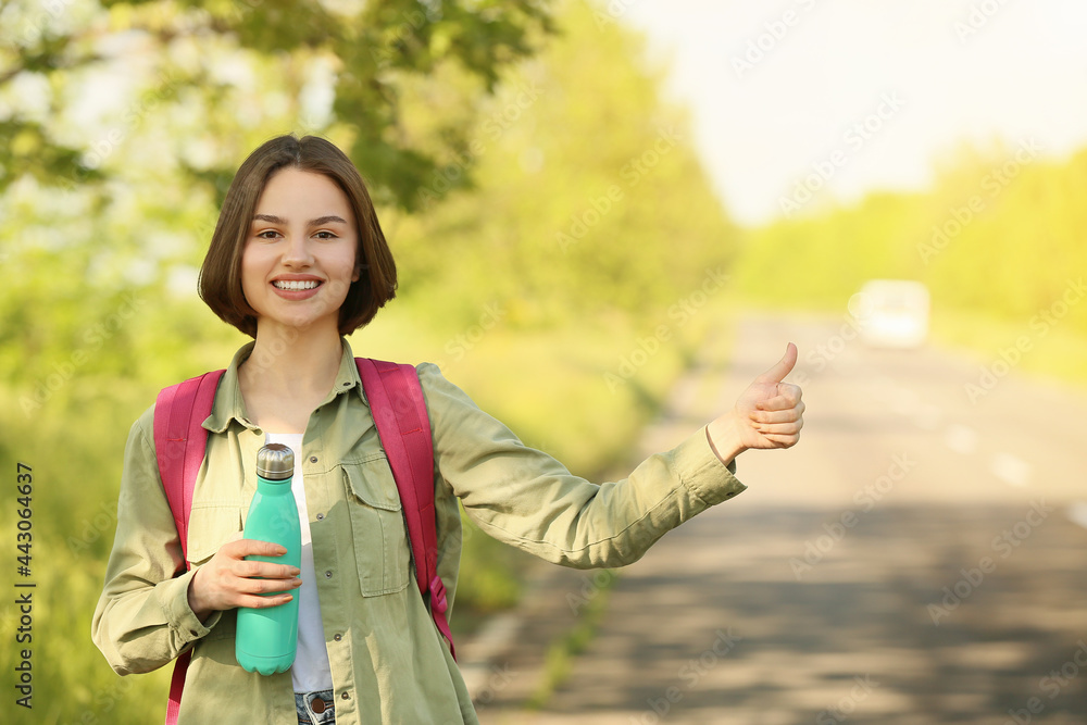 Young woman with bottle of water hitchhiking on road Young woman with bottle of water hitchhiking on road
