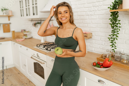 Happy smiling fit woman in activewear looking at camera while standing in the kitchen  after fitness workout at home.