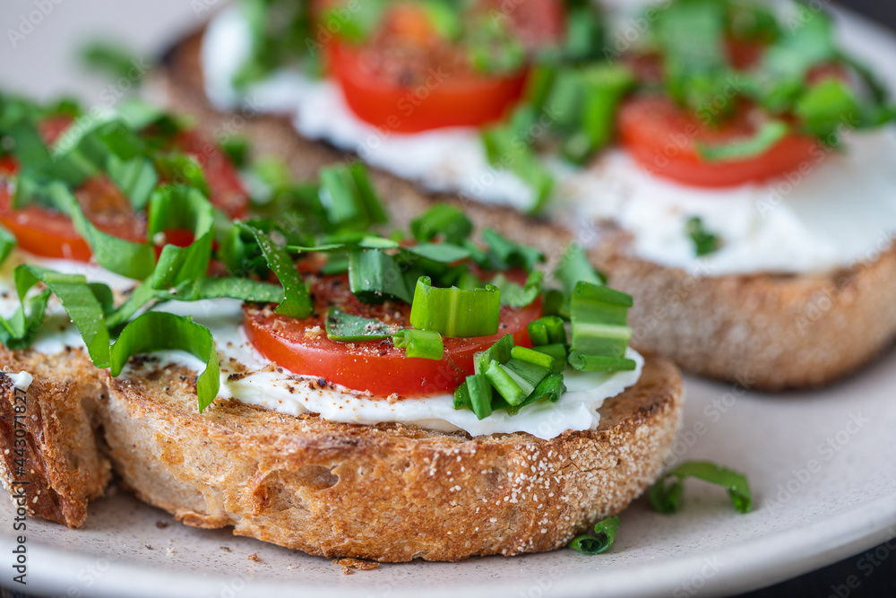 Delicious toasted bread with white cream cheese, green wild garlic and tomato on plate, close up Delicious toasted bread with white cream cheese, green wild garlic and tomato on plate, close up