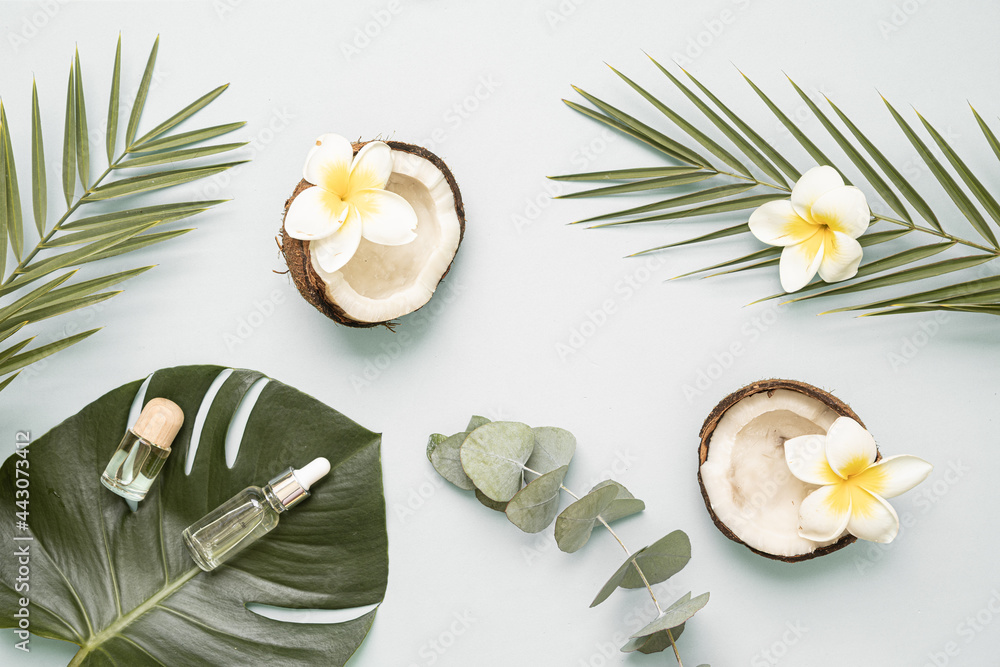 Coconut essential oil and palm leaf oil on a table with copy space on a pastel background. Styled composition of flat lay with tropical leaves and flowers. Coconut essential oil and palm leaf oil on a table with copy space on a pastel background. Styled composition of flat lay with tropical leaves and flowers.