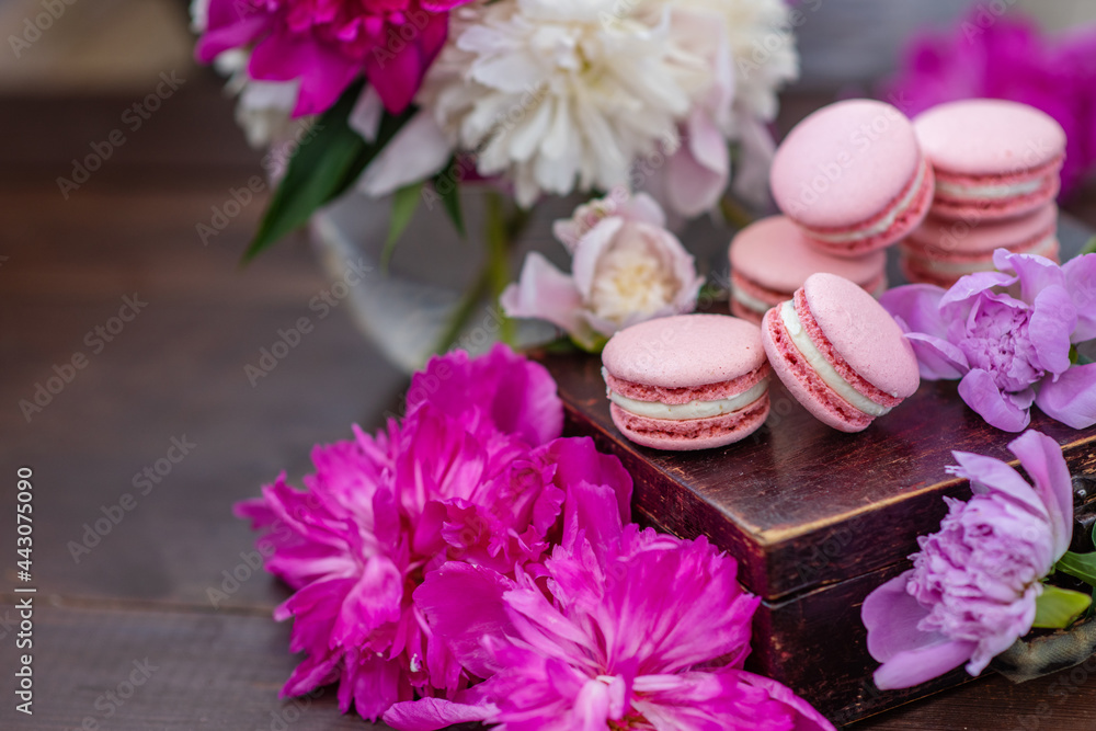 Pink macaroons lie on a wooden box surrounded by peony flowers Pink macaroons lie on a wooden box surrounded by peony flowers