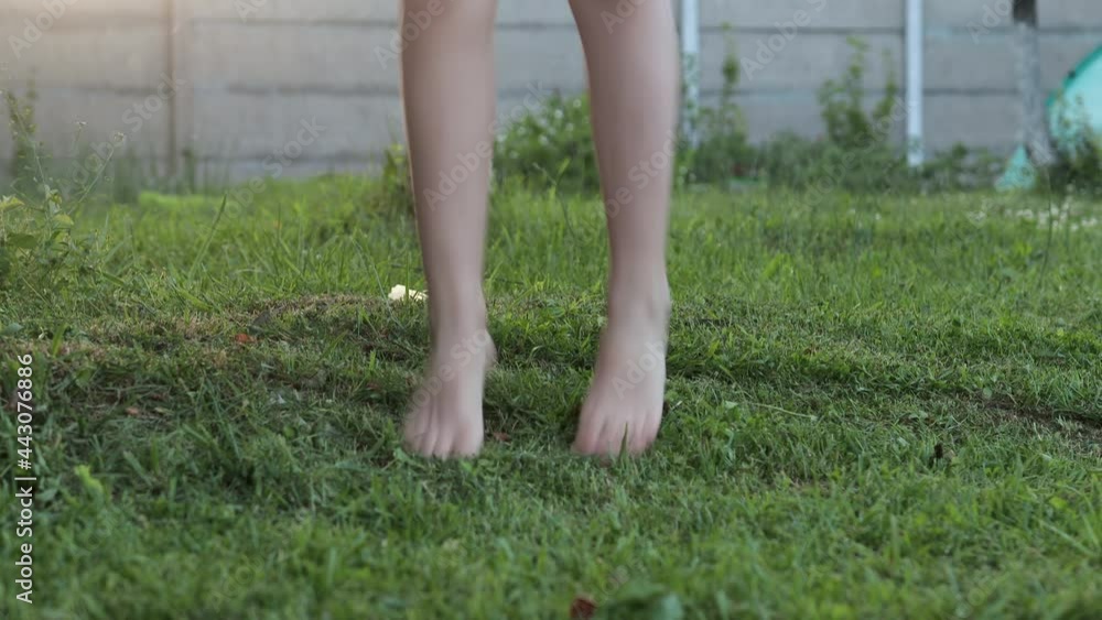 Close-up of the legs of a barefoot girl happily jumping on the fresh green grass in the countryside at sunset. Concept of childhood Close-up of the legs of a barefoot girl happily jumping on the fresh green grass in the countryside at sunset. Concept of childhood