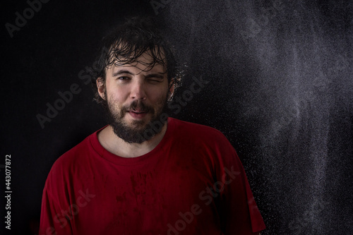 Portrait of a young dark-haired man with a beard with wet hair on a dark background with water drops
