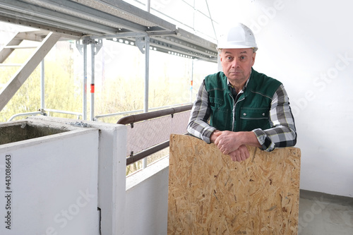 funny elderly builder with building materials in a white helmet protection and working uniform works at a construction site for the construction and repair of buildings