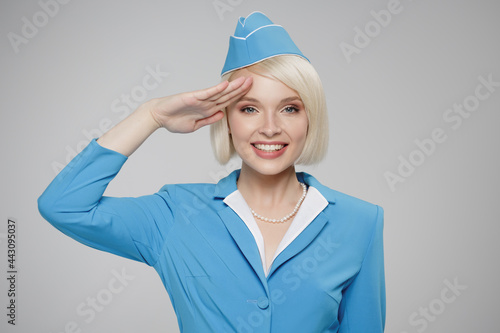 Attractive blonde flight attendant salutes. Gray background.