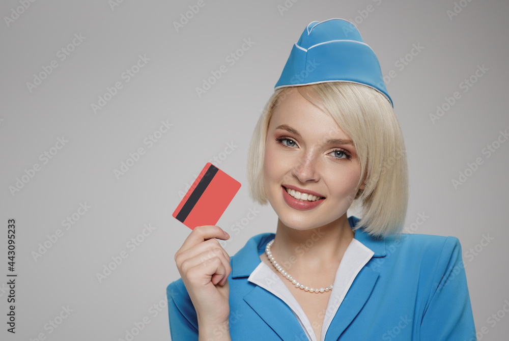 Smiling blonde stewardess holding credit card in her hand. Gray background. Smiling blonde stewardess holding credit card in her hand. Gray background.