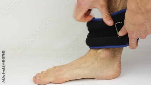 man puts on ankle weights on bare leg on white background, equipment for home sport or workout or fitness training