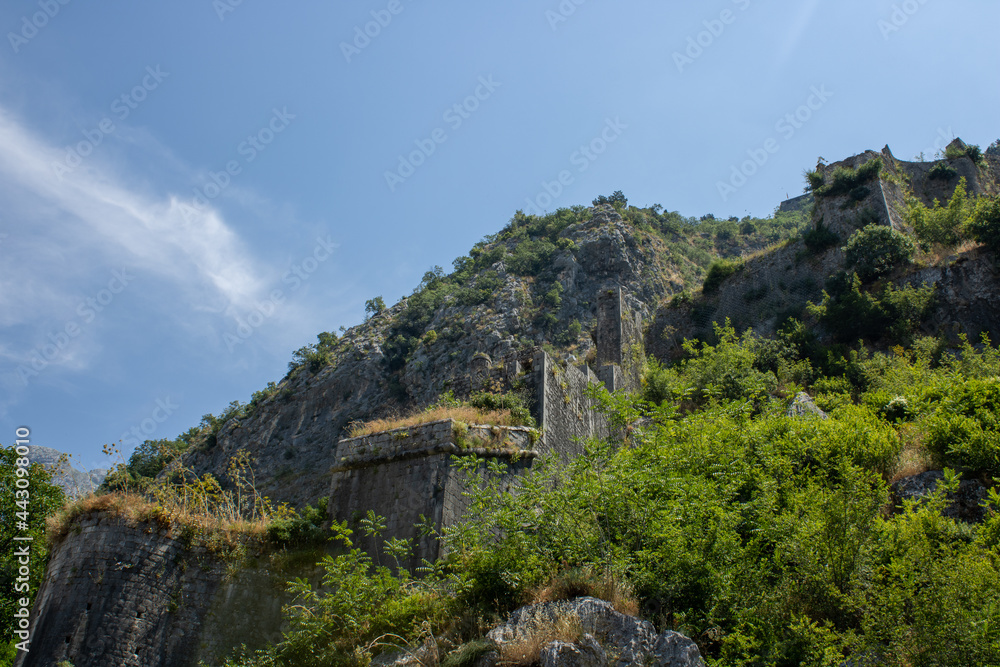 Ancient fortress on background of famous tourist town Kotor Bay mountains and sky,  Montenegro. Old fortress in sunny dayon the backdrop of the mountains. Picturesque and gorgeous scene.