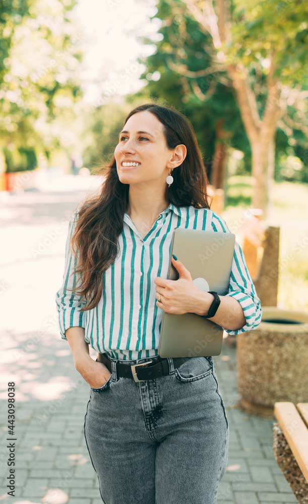 Portrait of a smiling girl holding laptop computer while walking outdoors Portrait of a smiling girl holding laptop computer while walking outdoors