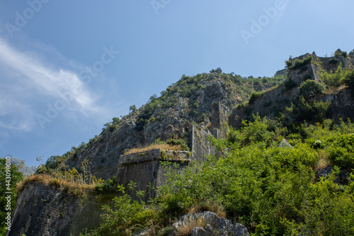 Ancient fortress on background of famous tourist town Kotor Bay mountains and sky   Montenegro. Old fortress in sunny dayon the backdrop of the mountains. Picturesque and gorgeous scene.