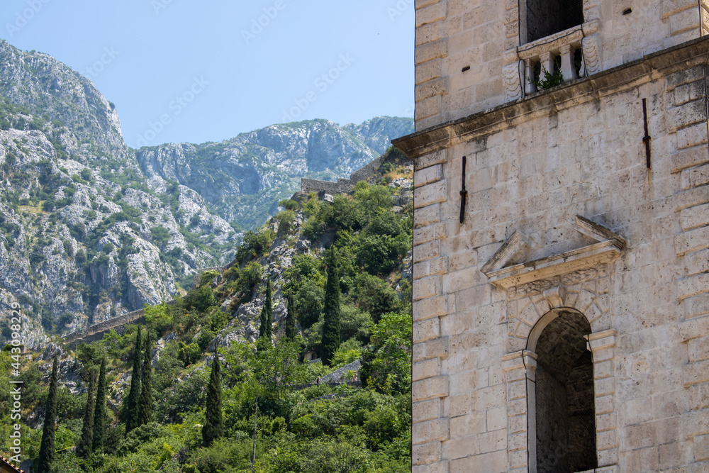 Church towers visible against the backdrop of a mountain landscape and green trees. Old medieval church in backdrop of the mountains in Kotor Montenegro