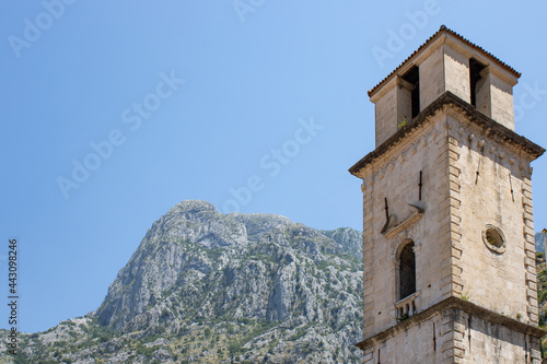 Church towers visible against the backdrop of a mountain landscape and green trees. Old medieval church in backdrop of the mountains in Kotor Montenegro