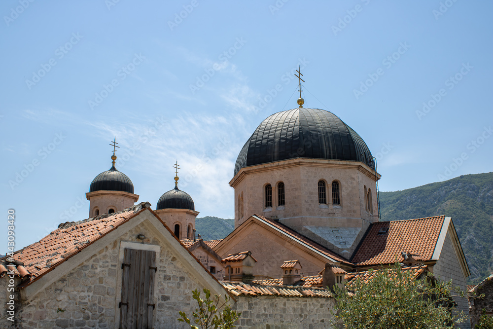 Church towers visible against the backdrop of a mountain landscape and green trees and sky. Old medieval church in backdrop of the mountains in Kotor Montenegro