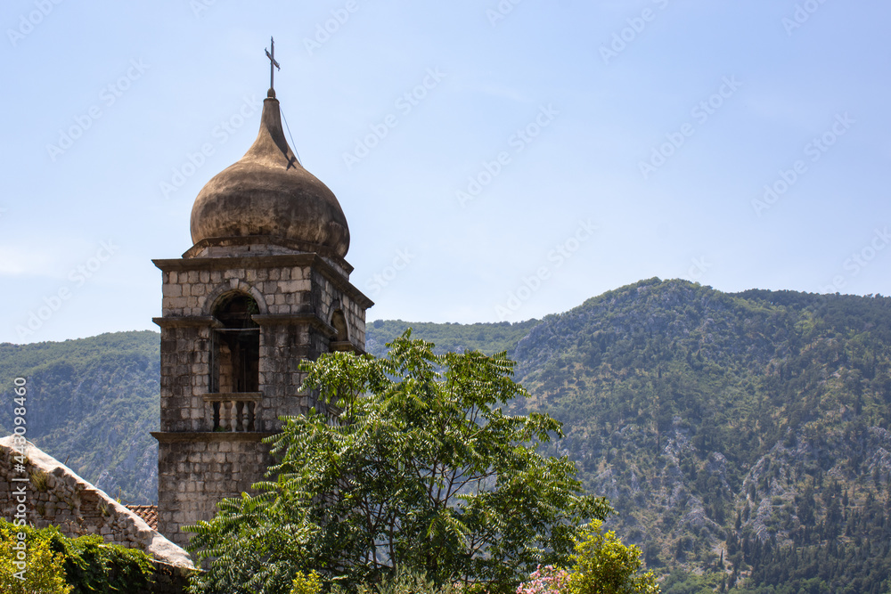 Church towers visible against the backdrop of a mountain landscape and green trees. Old medieval church in backdrop of the mountains in Kotor Montenegro