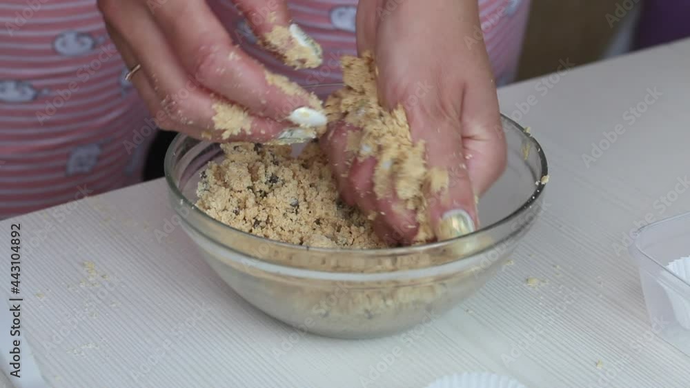 A woman mixes peanut butter, chocolate and coconut flour with her hands to make sweets. Nearby on the table are paper candy tartlets. Close-up shot. A woman mixes peanut butter, chocolate and coconut flour with her hands to make sweets. Nearby on the table are paper candy tartlets. Close-up shot.