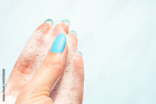 female fingers in white soapy foam on a blue background