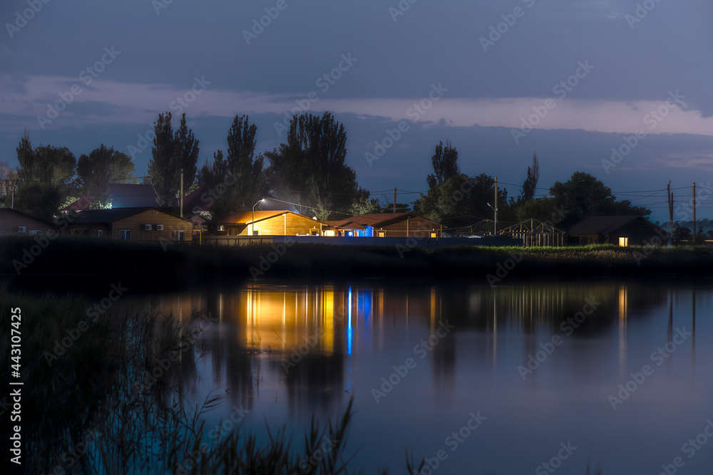 Landscape of the night city on the water, the reflection of lonely glowing houses in the water.