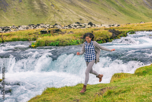 Woman joyful cheerful happy aspirational joyous smiling laughing having fun by waterfall on Iceland. Girl tourist in casual clothing visiting icelandic nature landscape