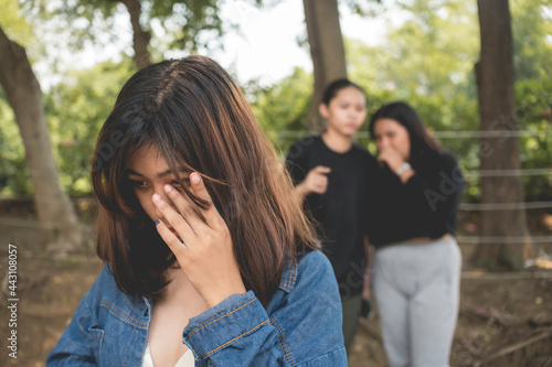 A young woman sobs aware of two women making fun of her and spreading false gossip. Bullying in female teens. photo