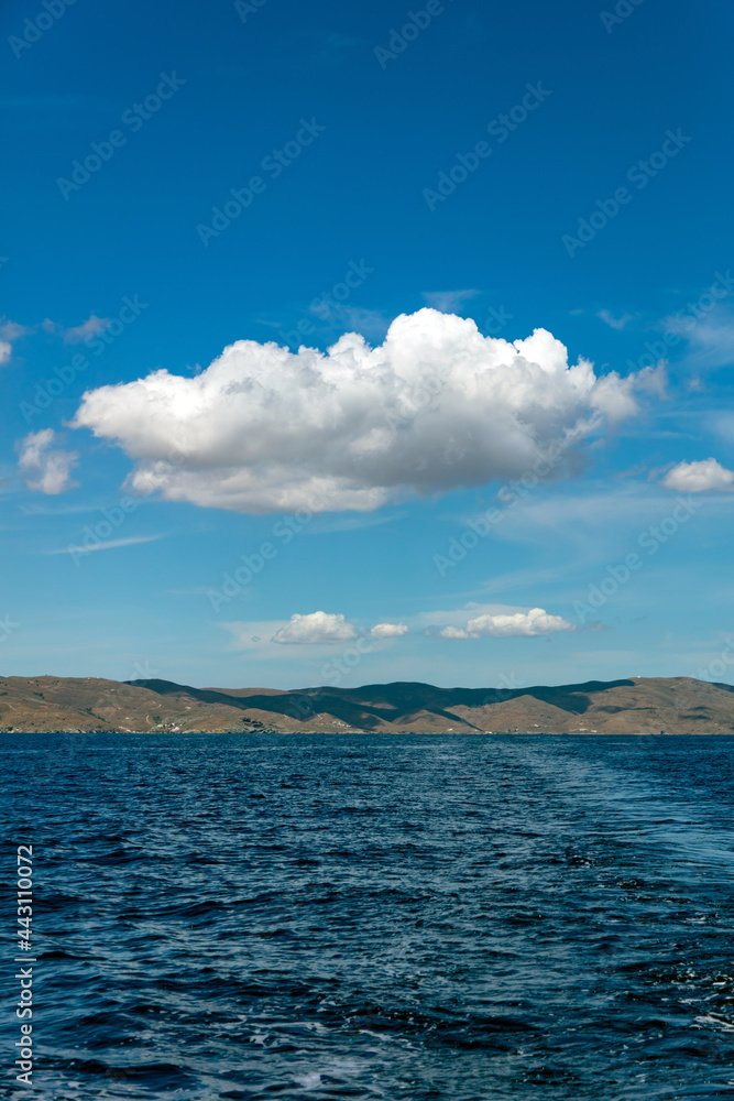 Rocky land, rippled sea, cloud on clear blue sky. Aegean sea, Cyclades