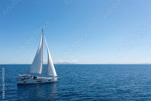 Sailing boat with open white sails, blue sky and rippled sea background