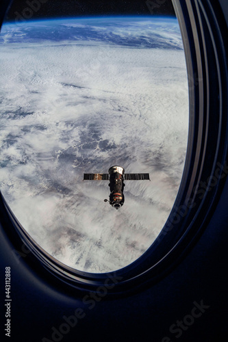 View on ISS Progress resupply ship, View out from a passenger window on the SpaceX Crew Dragon. Docking maneuver near the Space Station. Elements of image furnished by NASA photo