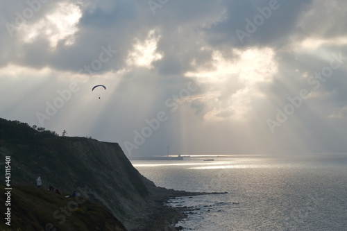 Parapentista en acantilados de Azkorri, Getxo, Bizkaia, España. Con rayos de sol a su espalda entre las nubes.  photo