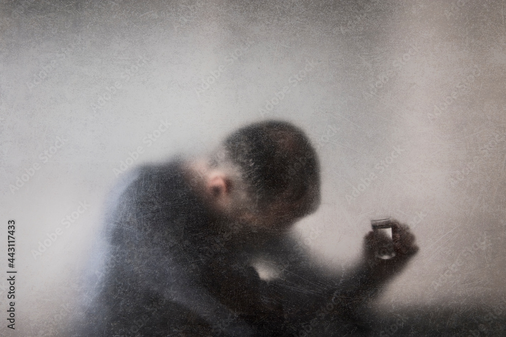 Man with a glass of vodka behind a dusty scratched glass. Alcoholism concept.