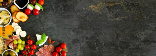Italian theme charcuterie corner border against a dark slate banner background. Selection of cheese, meat and fruit appetizers. Above view with copy space. photo