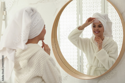 Beautiful young woman doing facial massage with gua sha tool in front of mirror at home photo